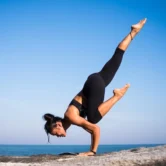 lady doing a yoga stretch on a rock by the water