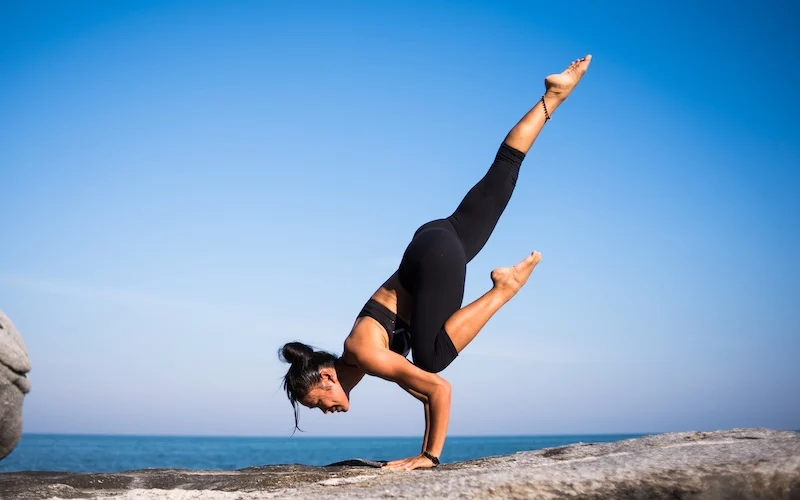 balance lady doing a yoga stretch on a rock by the water